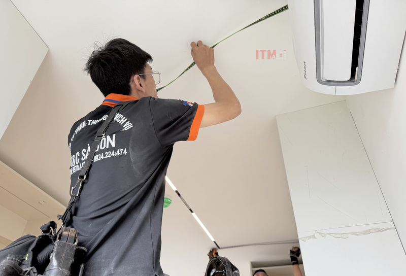 Kỹ thuật viên đo vị trí trên trần có hệ đèn tuyến tính và điều hòa trước khi lắp loa.