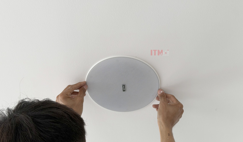 Kỹ thuật viên hoàn thiện mặt loa sát trần, giữ viền gọn và mặt lưới đúng vị trí.