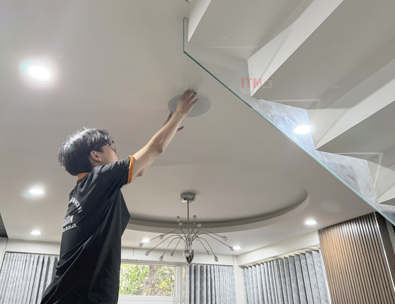 Kỹ thuật viên T&C mặc đồng phục gọn gàng kiểm tra mặt loa âm trần trong phòng khách